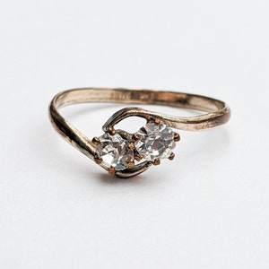 Op de afbeelding: Een zilveren ring met twee heldere stenen gezet in een gedraaide band.