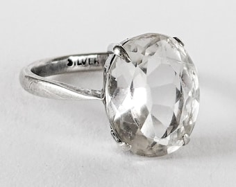 Könnte beinhalten: Ein silberner Ring mit einem ovalen, klaren Edelstein. Das schmale Band trägt die Gravur "SILVER". Der facettierte Edelstein fängt das Licht ein.