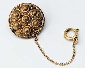 May include: A gold-toned metal button with a chain attached. The button has a circular design with eight raised circles.