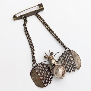 May include: A gold-toned metal brooch featuring a detailed butterfly design with a chain attached. The butterfly has a textured, openwork body and wings.