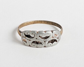 Könnte beinhalten: Ein Vintage-Ring mit einem goldfarbenen Band und einem silberfarbenen, strukturierten Design. Der silberne Bereich weist eine Reihe von verbundenen, oval geformten Mustern auf. Der Ring ist vor einem schlichten weißen Hintergrund platziert.