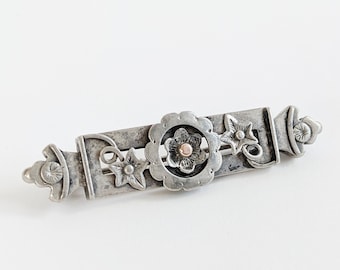Könnte beinhalten: Silberne Brosche mit floralem Design. Die Brosche zeigt eine zentrale Blume mit goldener Mitte und ist von kleineren Blumen und Blättern umgeben.