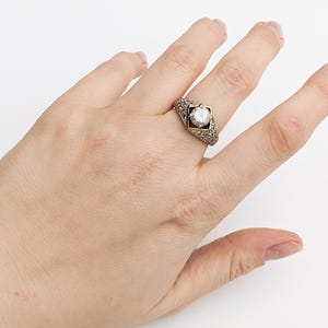Op de afbeelding: Een gouden ring met een grote, heldere edelsteen gezet in een geometrisch ontwerp. De ring is bezet met kleinere edelstenen rond de hoofdsteen.