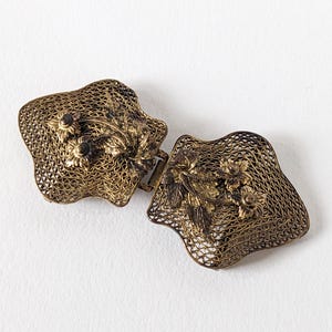 Puede incluir: Una taza de cerámica blanca con un asa negra y el texto "But First, Coffee" en negrita negra. La taza se encuentra sobre un fondo borroso, sugiriendo un ambiente acogedor.