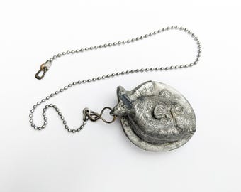 Könnte beinhalten: Eine silberne Kette mit einem Metallanhänger in Form eines Fisches. Der Fisch ist mit Schuppen und Flossen verziert.