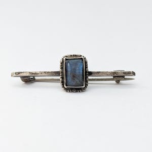 Può includere: Un fermaglio d'argento con una pietra preziosa rettangolare blu incastonata in una cornice d'argento.