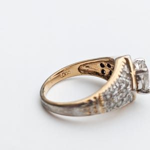 Op de afbeelding: Een gouden en zilveren ring met een grote, heldere steen en kleinere stenen die in de band zijn gezet. De ring is aan de binnenkant gemarkeerd met "925".