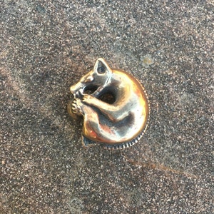 Könnte beinhalten: Ein goldfarbener Metallring mit einer detaillierten Skulptur eines zusammengerollten Fuchses.