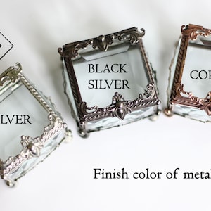 May include: Three small, square glass boxes with ornate metal frames in silver, black silver, and copper finishes. The boxes have hinged lids and are labelled with their respective metal finish colours. The Nimbus logo is in the upper left corner.