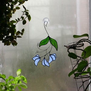May include: A stained glass window hanging with a blue and green floral design. The hanging is attached to a window with a suction cup.