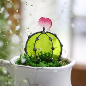 May include: A small green glass cactus with a pink glass flower on top, sitting in a white ceramic pot with green moss.
