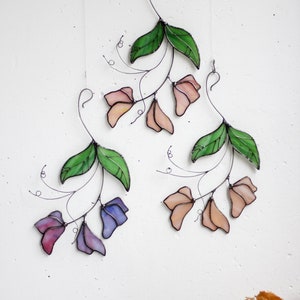 May include: Three stained glass flower wall hangings with green leaves and pink, peach, and purple flowers.