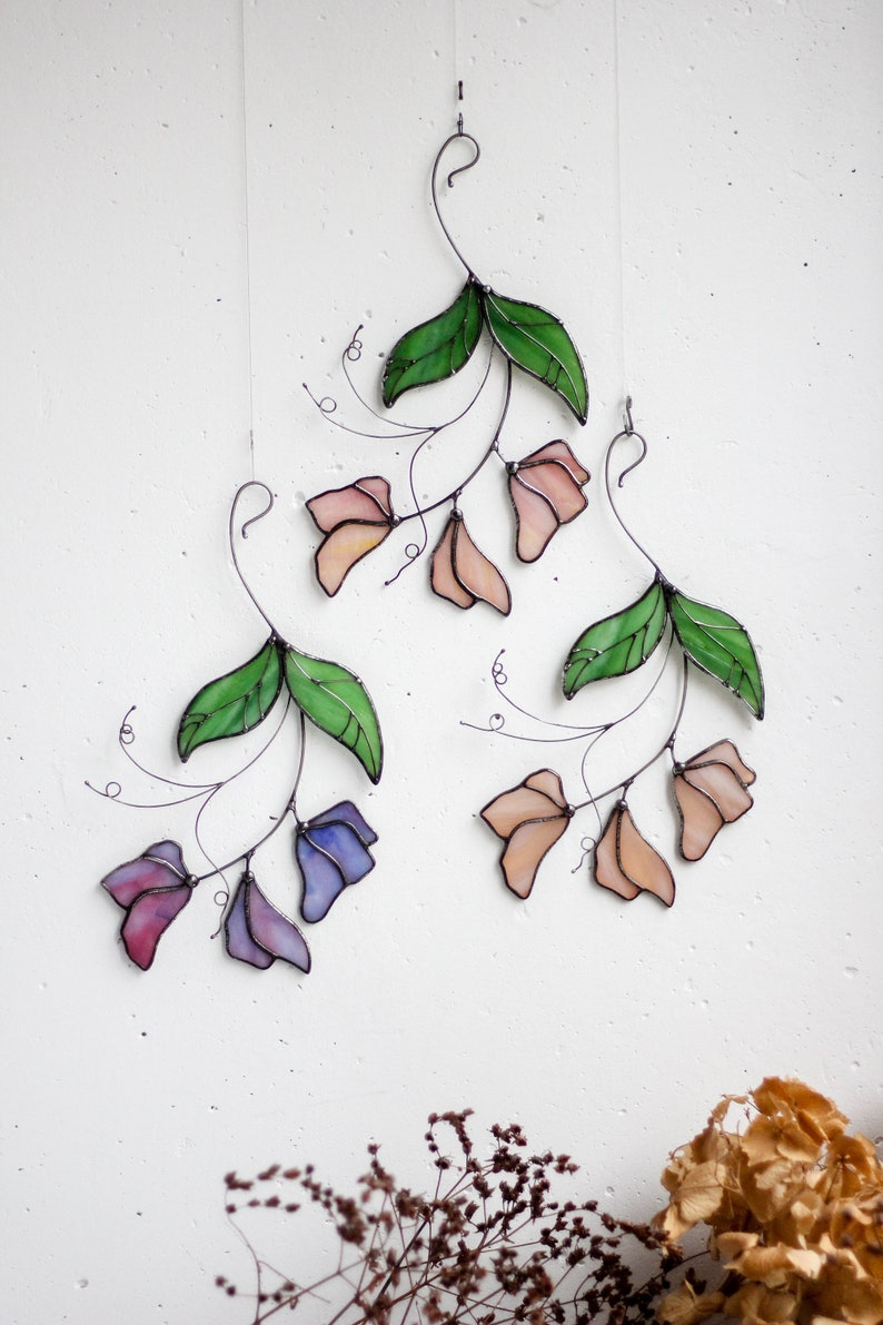 May include: Three stained glass flower wall hangings with green leaves and pink, peach, and purple flowers.