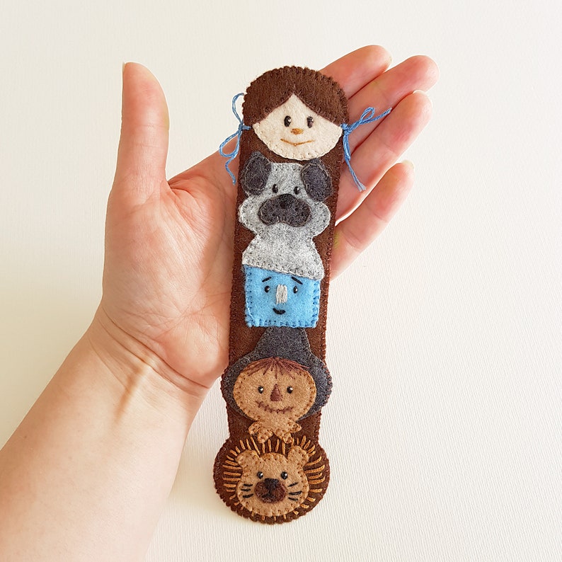 May include: A felt finger puppet set featuring characters from the Wizard of Oz. The set includes Dorothy, Toto, the Scarecrow, the Tin Man, and the Cowardly Lion. Each puppet is made of felt and has embroidered details.