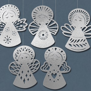 May include: Five silver paper angel ornaments with different designs. Each angel has a halo, wings, and a dress. The angels are hanging from strings.