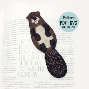 Könnte beinhalten: Ein Filz-Biber-Lesezeichen mit braunem Körper, schwarzen Augen und weißem Bauch. Das Lesezeichen befindet sich auf einer Buchseite mit dem Text "You'd be off, don't want the troll to gobble you up," said the princess."