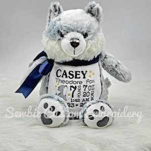 May include: A plush gray and white wolf stuffed animal with a navy blue ribbon. The wolf has embroidered details and a personalized panel with the name "Casey", birth details, and a small illustration.