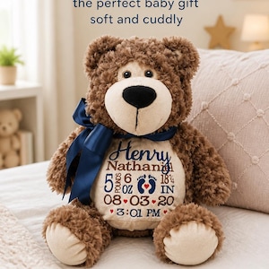 May include: A brown plush teddy bear with a navy blue satin ribbon around its neck. The bear features a cream-colored belly patch embroidered with the name Henry Nathan, birth details including 5 pounds 6 ounces, 18.25 inches, and 08-03-20 at 3:01 PM.