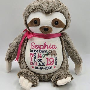 May include: A plush brown sloth toy with a white belly featuring embroidered pink and dark blue text: Sophia, Louise Blum, 7 pounds 14 oz, 12:11 AM, 19 inches, and 10-19-2026. A small sloth illustration is included, and a pink ribbon is tied around its neck.