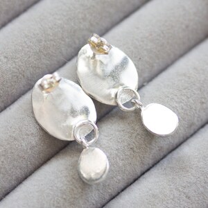 May include: A pair of silver dangle earrings with a smooth, oval-shaped top and a smaller round drop. The earrings have a hammered texture.