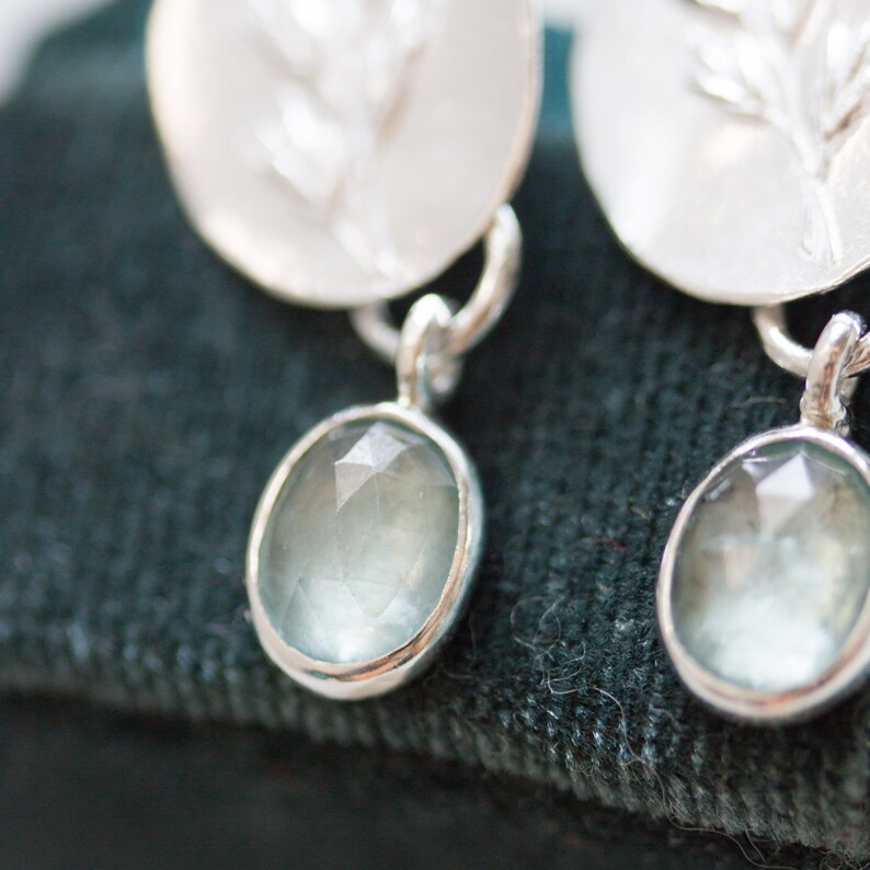 May include: A pair of silver earrings with a delicate branch design and a light blue gemstone dangle.