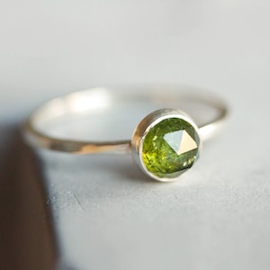 Op de afbeelding: Een zilveren ring met een groene edelsteen in een bezel-setting. De ring heeft een gehamerde textuur.