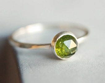 May include: A silver ring with a green gemstone set in a bezel setting. The ring has a hammered texture.