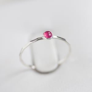 Puede incluir: Un anillo de banda de plata simple con una pequeña piedra preciosa redonda de color rosa.