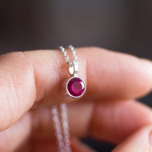 Puede incluir: Un collar de cadena de plata con un pequeño colgante redondo de piedra roja.