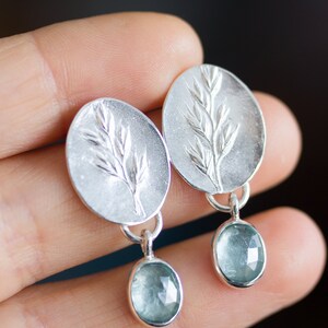 May include: A pair of silver earrings with a delicate leaf design and a light blue gemstone dangle.