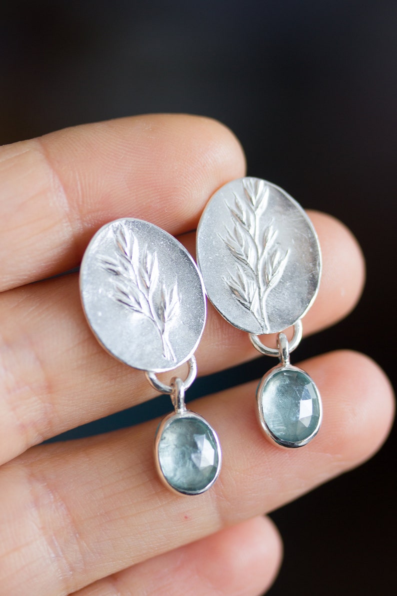 May include: A pair of silver earrings with a delicate leaf design and a light blue gemstone dangle.