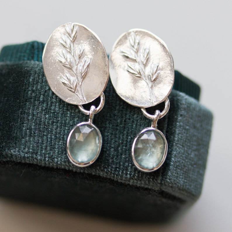 May include: Silver earrings with a delicate branch design and light blue gemstone drops.