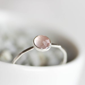 Könnte beinhalten: Ein silberner Ring mit einem hellrosa Rosenquarz-Edelstein. Der Ring ist schlicht und elegant.