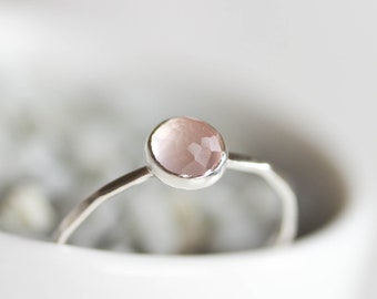 Puede incluir: Un anillo de plata con una piedra preciosa de cuarzo rosa claro. El anillo es simple y elegante.