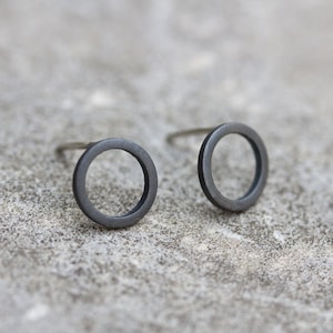 May include: A pair of black circle stud earrings. The earrings are made of metal and have a simple, minimalist design.