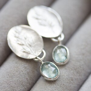 May include: Silver earrings with a delicate leaf design and a light blue gemstone dangle.