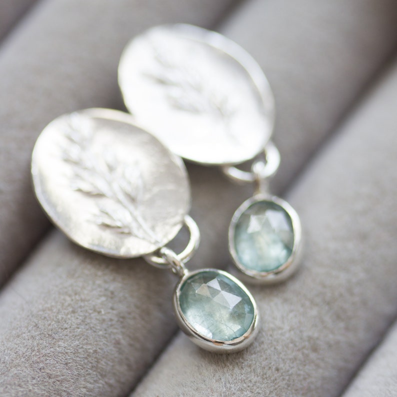May include: Silver earrings with a delicate leaf design and a light blue gemstone dangle.