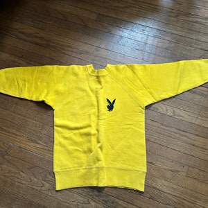May include: A yellow sweatshirt with a black Playboy bunny logo on the front.