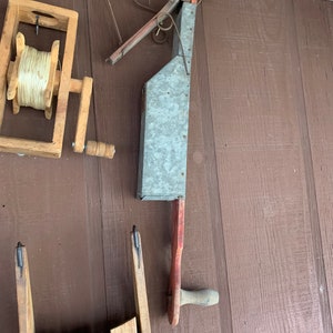 May include: A vintage wooden seed planter with a metal seed hopper and a wooden handle. The planter is attached to a wooden spool with twine.