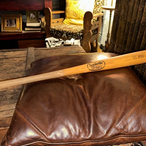 May include: A wooden Louisville Slugger tee ball bat with the text "Louisville Slugger" and "Tee Ball" printed on it.
