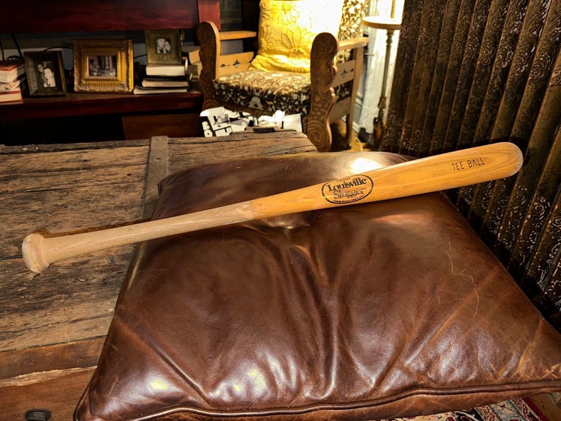 May include: A wooden Louisville Slugger tee ball bat with the text "Louisville Slugger" and "Tee Ball" printed on it.