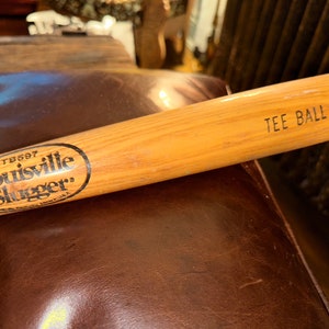 May include: A wooden Louisville Slugger tee ball bat with the text "TB697" and "Louisville Slugger" in a circle. The bat is labelled "Tee Ball" on the end.