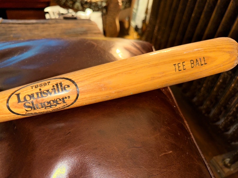 May include: A wooden Louisville Slugger tee ball bat with the text "TB697" and "Louisville Slugger" in a circle. The bat is labelled "Tee Ball" on the end.