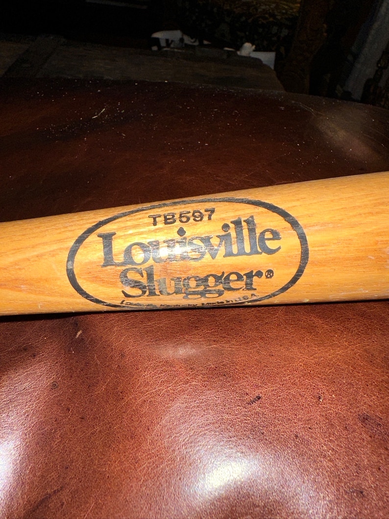 May include: A wooden Louisville Slugger baseball bat with a black oval label that reads "Louisville Slugger" and "TB597".