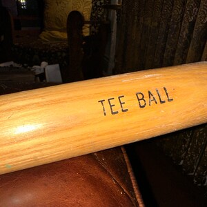May include: A wooden tee ball bat with the words "TEE BALL" printed on the side.