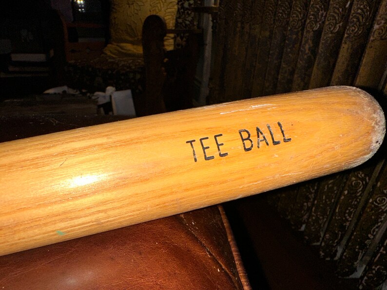 May include: A wooden tee ball bat with the words "TEE BALL" printed on the side.