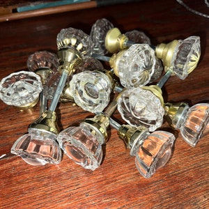 May include: A collection of vintage glass door knobs with brass hardware. The knobs are clear glass with a faceted design.