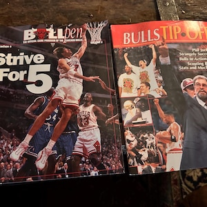 May include: Two vintage Chicago Bulls basketball game programs. The left program is titled "Bulls Ben" with "Strive For 5" in large white text. The right program is titled "Bulls Tip-Off" with images of players and coaches.