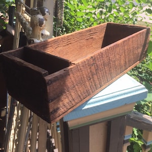 May include: A rustic wooden planter box with a divided section. The box is made of weathered wood and has a natural brown color.