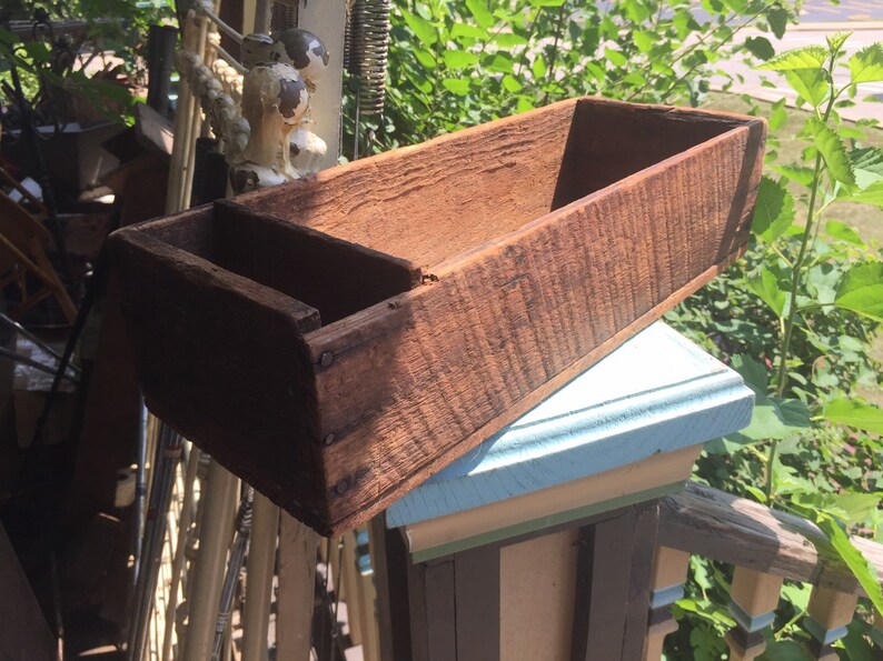 May include: A rustic wooden planter box with a divided section. The box is made of weathered wood and has a natural brown color.